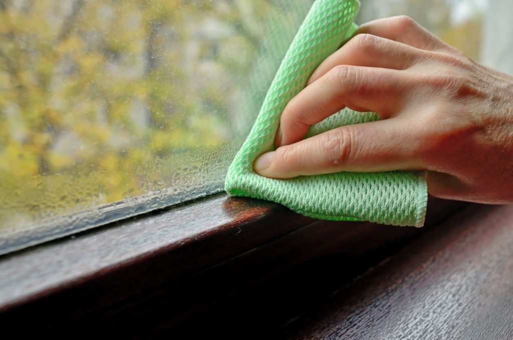 hand with green cloth wiping bottom of window