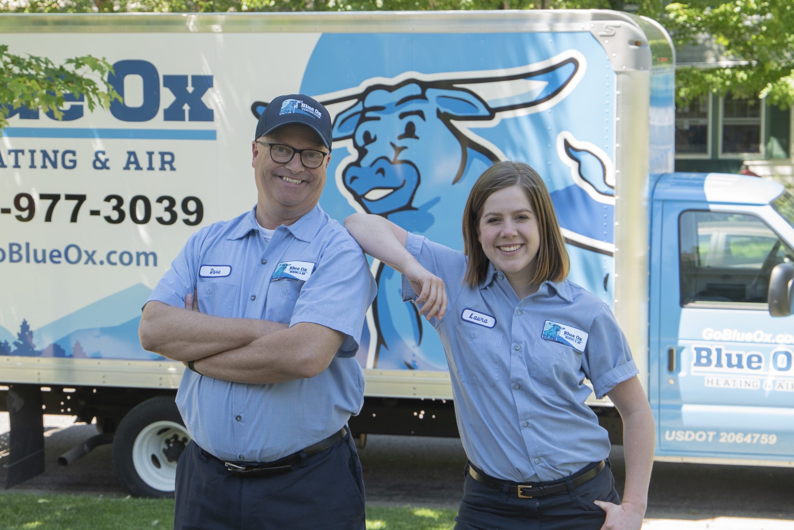 two plumbers with woman's are on man'ss shoulder with box truck behind them