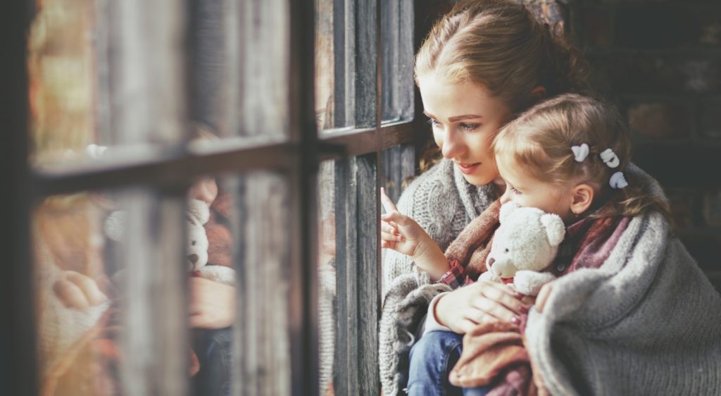 woman and girl looking out window with blanket wrapped around them